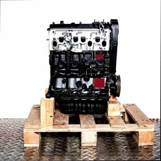 Engine 1X on wooden pallet against white background. Black and silver engine with intake manifold and parts in plastic bag, standing upright.
