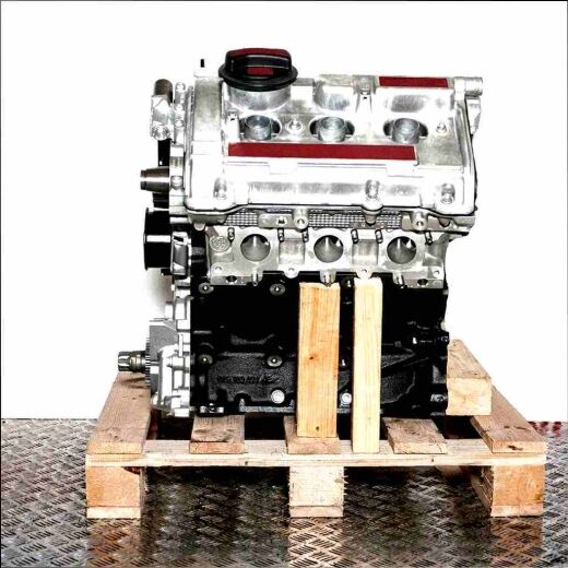 ACK engine on a wooden pallet against a white background. The silver cylinder head and black engine block are visible.