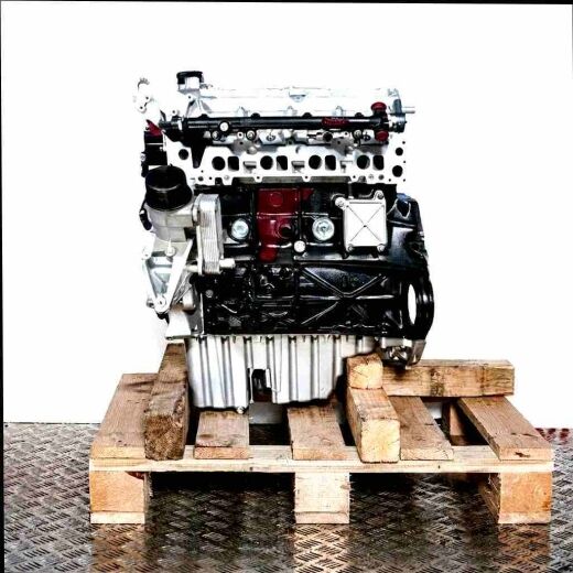 Side view of an OM 611.981 engine on a wooden pallet against a white background. The silver and black engine with yellow accents and hoses is vertically oriented.