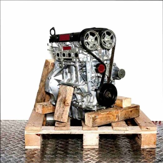 STJA engine on a wooden pallet against a white background. The silver engine, featuring a black cylinder head cover and timing belt system, is displayed in detail.