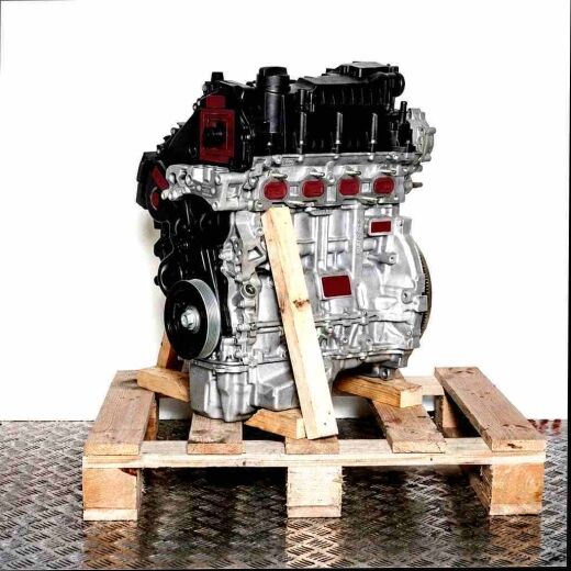 Side view of engine XUJA on a wooden pallet against a white background. The engine, featuring silver and black components, is vertically oriented.